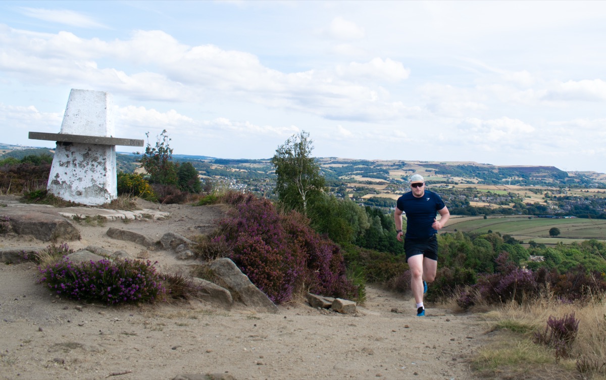 Shea running uphill beside a countryside trig point