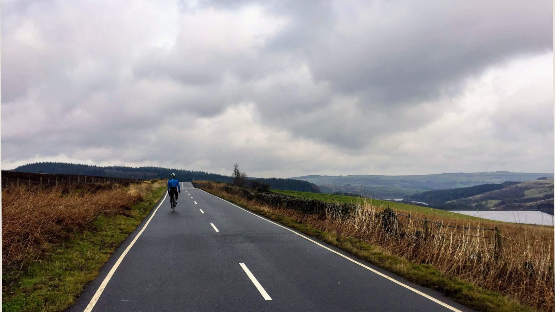 A cyclist riding along a quiet countryside road under a cloudy sky